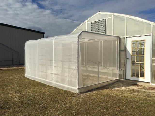 An insect screen room on the outside of a greenhouse.