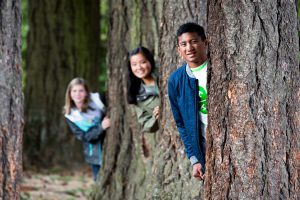 picture of three youth peeking from behind a tree