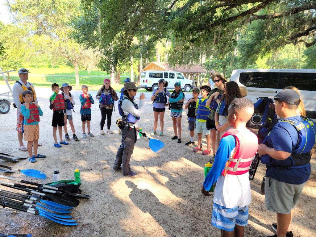 group of youth surrounding an adult as she gives instructions before the paddling trip.