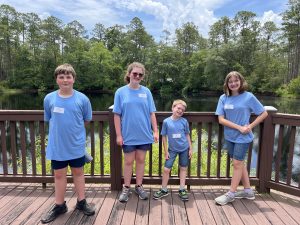 Photo of four Okaloosa 4-H County youth in front of a lake in Austin Cary Forest before the 2025 Florida 4-H Forest Ecology Contest.