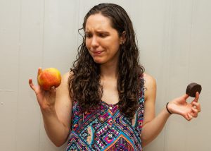 Confused woman choosing between apple and snack cake