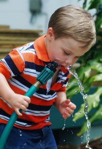 little boy drinking from water hose