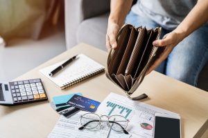 woman holding open an empty wallet over a clutter of financial papers