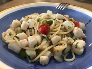 A blue bowl filled with bay scallop linguini in a white wine garlic sauce.