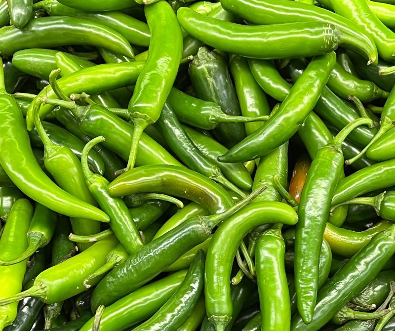 Fresh serrano peppers in shades of vibrant green, with smooth, elongated, and slightly curved shapes.