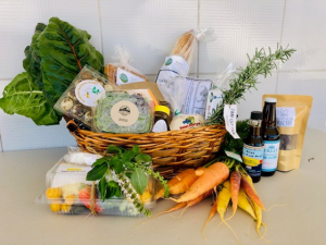 A basket filled with fresh produce, baked goods, and local products from multiple farmers, prepared for an online pre-order.